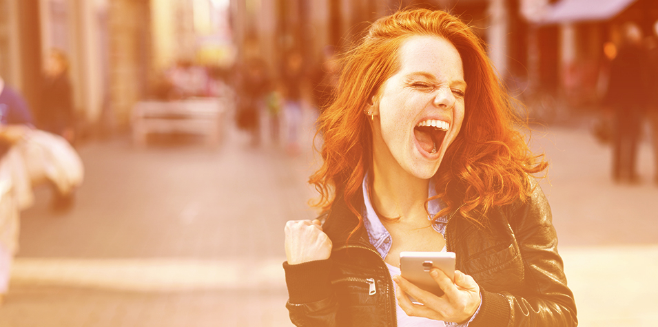 a woman holding a mobile phone, smiling and pumping her fist